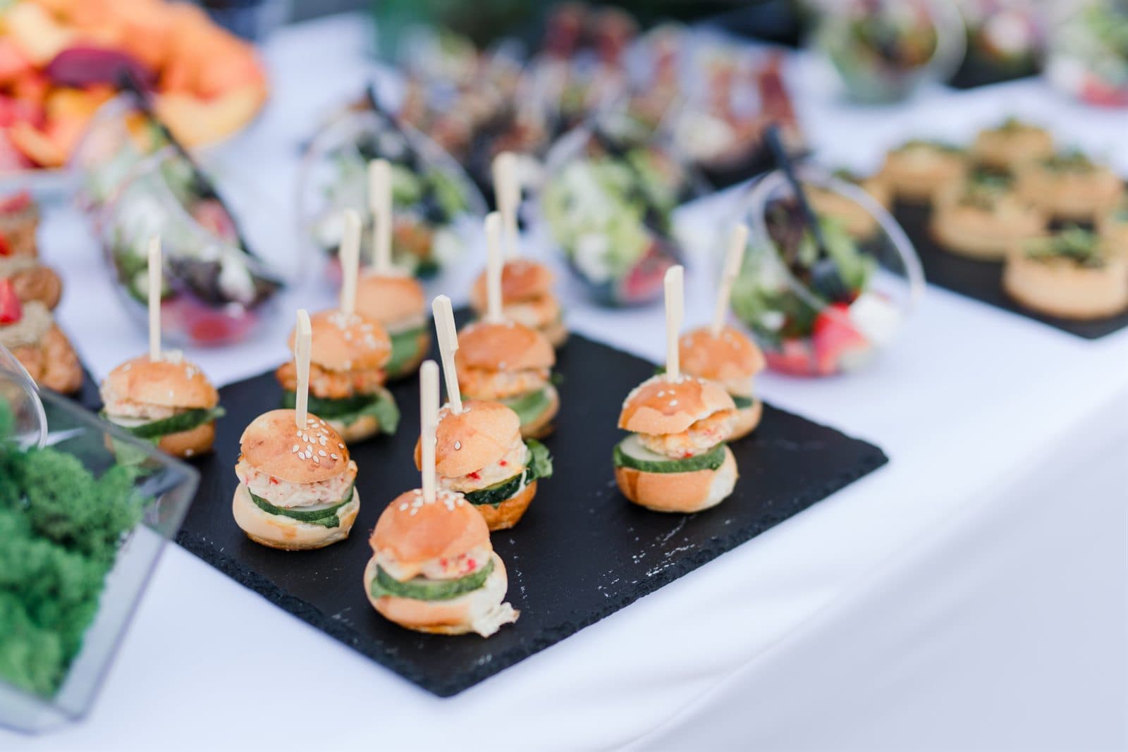 A slate board of miniature sliders and canapés on a dressed table